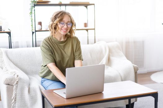 Woman with glasses use laptop typing keyboard sitting couch big window background home interior Freelance female working from home Distance learning student relaxing watch lessons video conference.