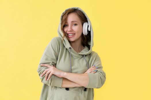 Happy teeth smile woman listen music headphones Caucasian female enjoy podcast or audio books dressed oversize hoodie yellow background close up portrait