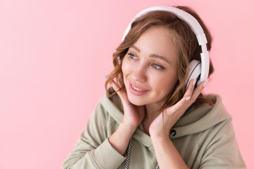 Happy teeth smile woman listen music headphones Caucasian female enjoy podcast or audio books dressed oversize hoodie pink background close up portrait
