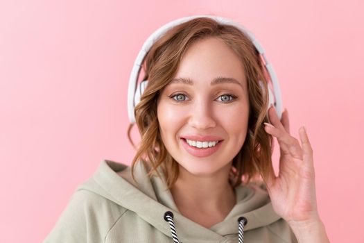 Happy teeth smile woman listen music headphones Caucasian female enjoy podcast or audio books dressed oversize hoodie pink background close up portrait