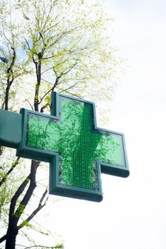 Green cross pharmacy symbol on blue sky background. No people