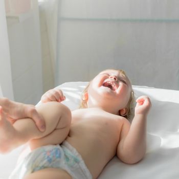 Mom does baby gymnastics for the baby's legs. Close-up. A happy child lies on his back.