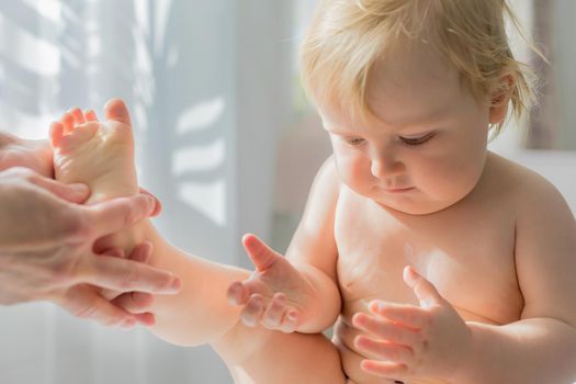 Mom gives her baby a leg and foot massage. Close-up. A satisfied baby is sitting on a massage table.