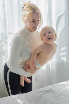 Mom does children's gymnastics for the baby, holding him by the chest. Close-up. Happy child is trying to climb.