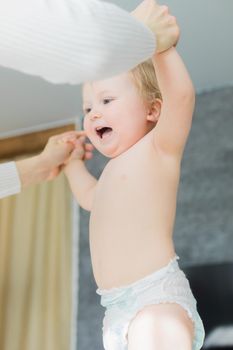 Mom does baby gymnastics for the baby's arms. Close-up. A happy child is standing at the table.