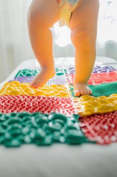 The kid walks barefoot on multi-colored massage rugs. Foot massage