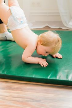 Mom holds the baby by the legs, the baby walks on the rug in her arms. Gymnastics for a child