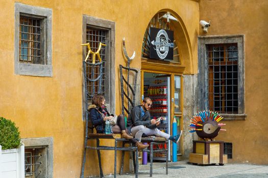 A girl and a guy are sitting on large chairs at the entrance to the pencil store. Prague, Czech Republic April 14, 2018
