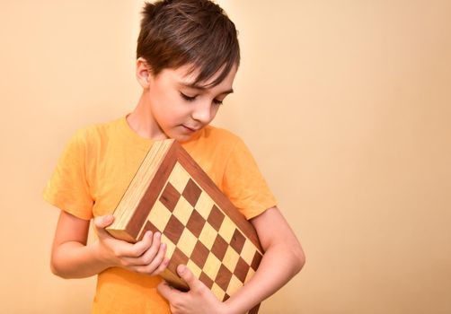 a boy holds a chessboard in his hands and looks at it.