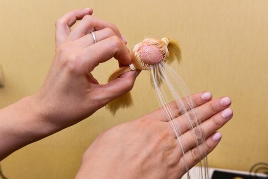 female hands and holding a doll head, how to make a doll hairstyle, hobby concept.