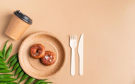 Knolling concept. Eco friendly zero waste disposable tableware top view flat lay on brown background. Craft paper plate with donuts, cup, fork and knife. Copy space