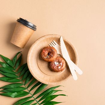 Knolling concept. Eco friendly zero waste disposable tableware top view flat lay on brown background. Craft paper plate with donuts, cup, fork and knife