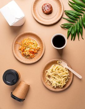 Knolling concept. Eco friendly zero waste disposable tableware with pasta, salad and donut top view flat lay on brown background