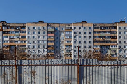 residential multi-storey building behind a fence with barbed wire at daylight, the concept of imprisonment, restriction of freedom, quarantine.