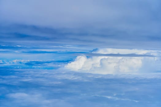 Landscape of fluffy white clouds on a dark blue sky. View from the plane at high altitude.