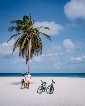 Eagle Beach Aruba, Palm Trees on the shoreline of Eagle Beach in Aruba, couple man, and woman on the beach of Aruba, couple with bycicle