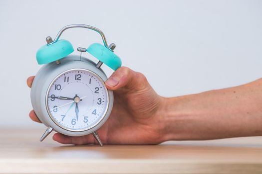 Male hand is holding a retro styled white alarm clock, isolated