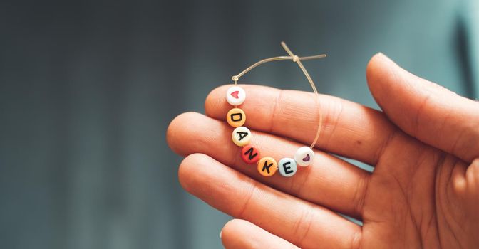 Close up of hand holding a bracelet made out of letters with the word “Danke”, close up