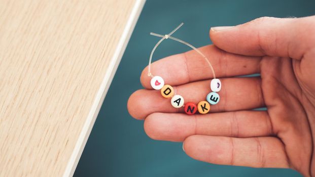 Close up of hand holding a bracelet made out of letters with the word “Danke”, close up