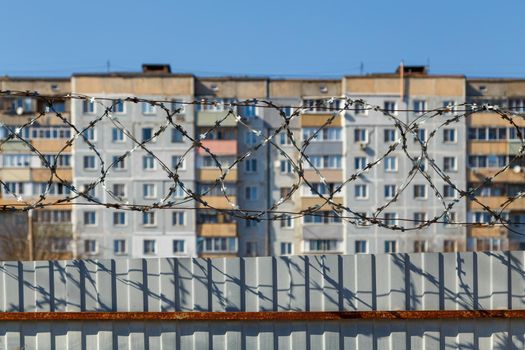 residential multi-storey building behind a fence with barbed wire at daylight, the concept of imprisonment, restriction of freedom, quarantine.