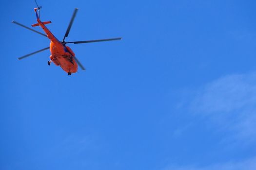 A red helicopter flies high in the blue sky, Aviation. High quality photo
