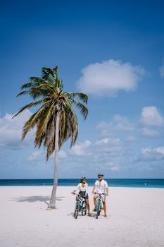 Eagle Beach Aruba, Palm Trees on the shoreline of Eagle Beach in Aruba, couple man, and woman on the beach of Aruba, couple with bycicle