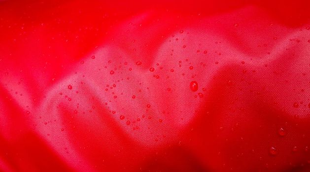 Large drops of water on a red textile with a waterproof effect. Water-repellent impregnation. Texture drops on the fabric.