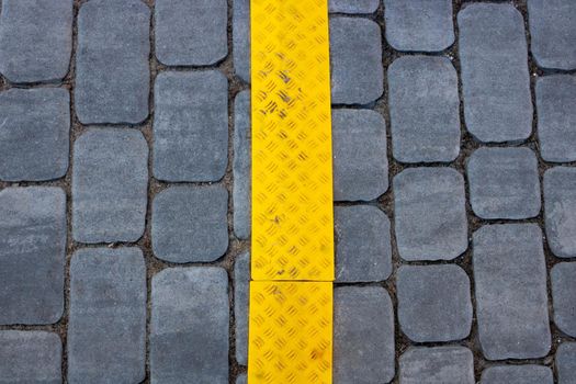 The texture of gray paving slabs with a yellow stripe on the street, a promising view. Cement brick square stone floor background. Sidewalk pavement pattern.