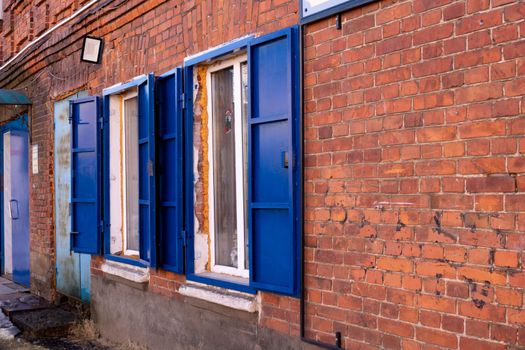 Side view, windows with blue iron shutters on a red brick wall.