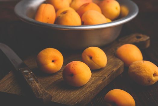 Mellow apricots with knife over old wooden cutting board and metal bowl with fruits