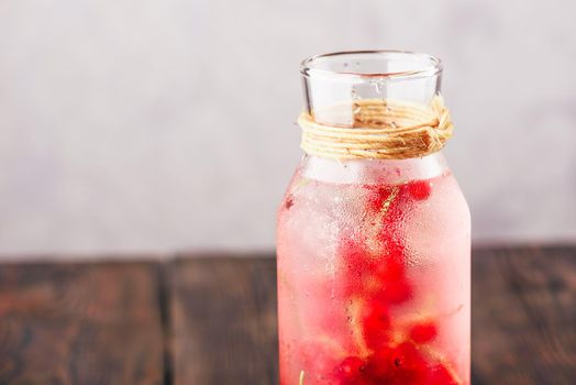 Red currant infused water with ice in glass bottle