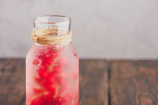 Red currant infused water with ice in glass bottle