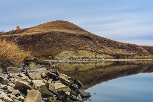 Hills on lakes coastline. Overcast sky reflected on the water surface