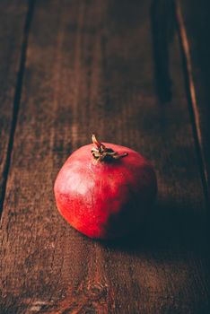 One red pomegranate on rustic wooden surface
