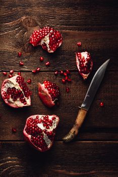 Pomegranate pieces with knife on rustic wooden surface. View from above