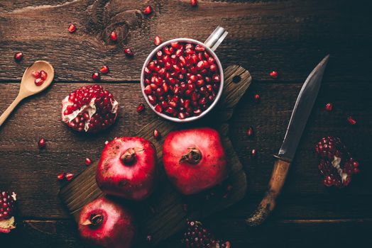 Metal mug full of pomegranate seeds. Whole fruits and pomegranate pieces on rustic wooden table. View from above