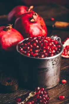 Metal mug full of the pomegranate seeds on rustic table