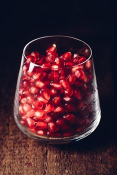 Glass full of red pomegranate seeds on wooden table