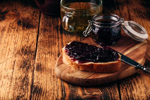 Toast with berry jam on cutting board and cup of green tea