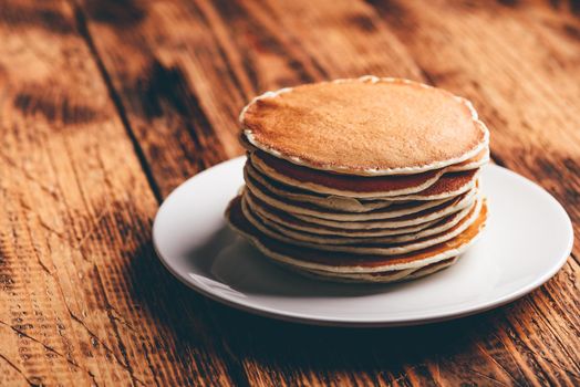 Stack of american pancakes on white plate over wooden table