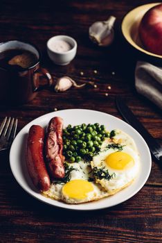 Breakfast with fried eggs, sausages and green peas on white plate