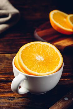 Sliced orange in a white cup on wooden surface