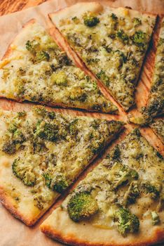 Slices of italian pizza with broccoli, pesto sauce and cheese on baking paper. High angle view