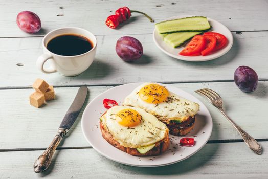 Bruschettas with vegetables and fried egg on white plate, cup of coffee and some fruits over wooden background. Healthy food concept.