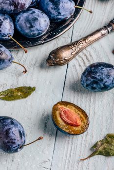 Ripe plums with sliced fruits, leaves and vintage knife over light wooden surface. View from above