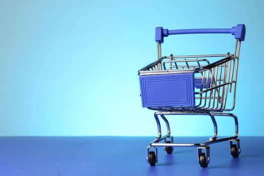 A miniature shopping cart over a blue background.