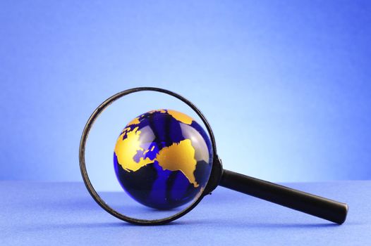 A magnify glass focused on a blue earth globe for searching world views concepts.