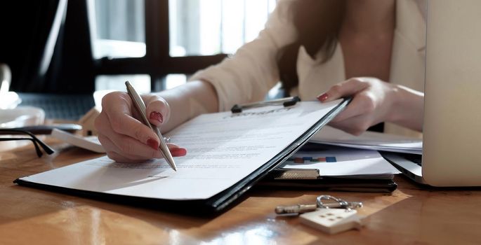 real estate agent assisting client to sign contract paper at desk with house model.