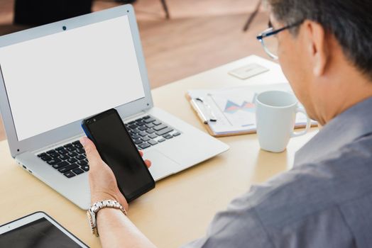 Old businessman using the mobile phone to video call conference on desk table at office. Asian senior business man working online on modern smartphone he looking at screen for remote online studying