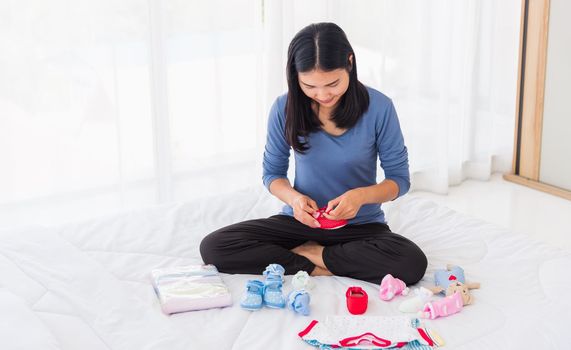 Asian mother preparing baby clothes resting and relaxing on the bed she makes purchase new baby clothes for after baby getting ready for newborn birth